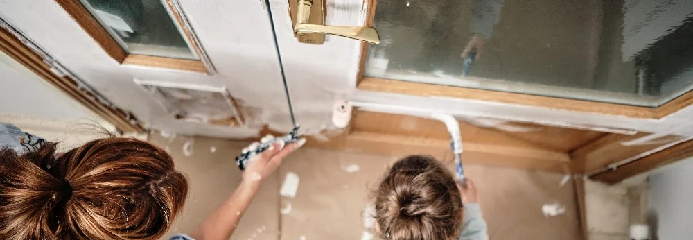 Zwei Personen streichen einen Türrahmen mit einer kleinen Farbrolle.